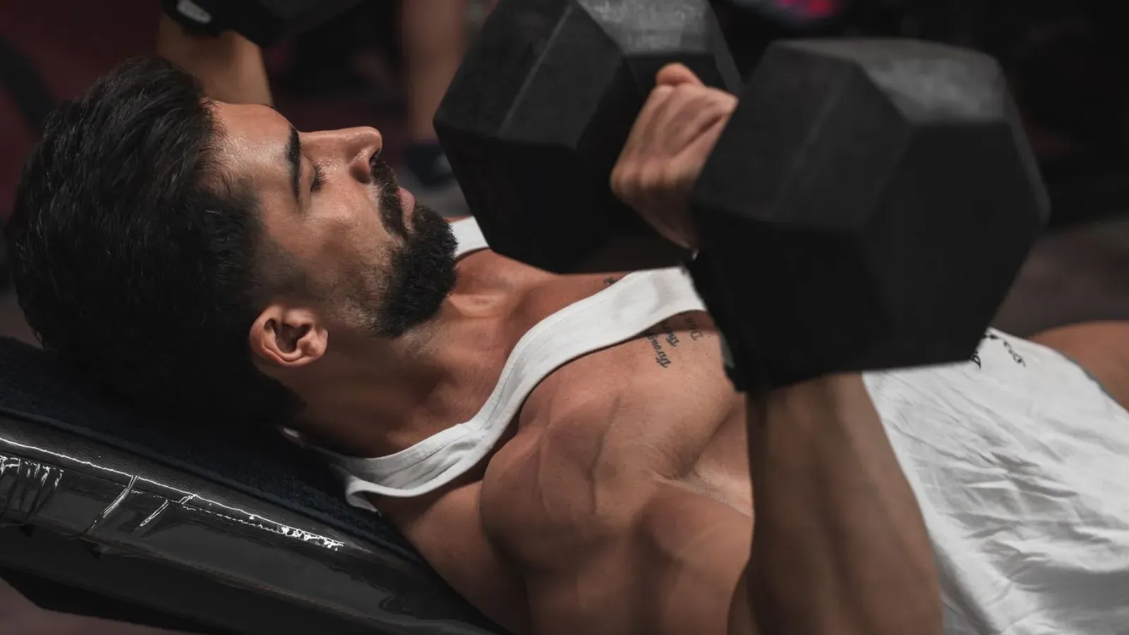 Pratiquant allongé sur un banc de musculation incliné réalisant un développé aux haltères