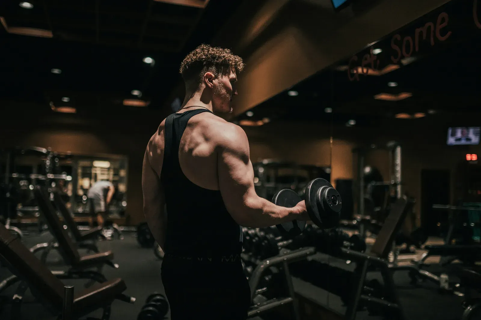 Pratiquant de musculation exécutant un curl haltère en salle, vu de dos