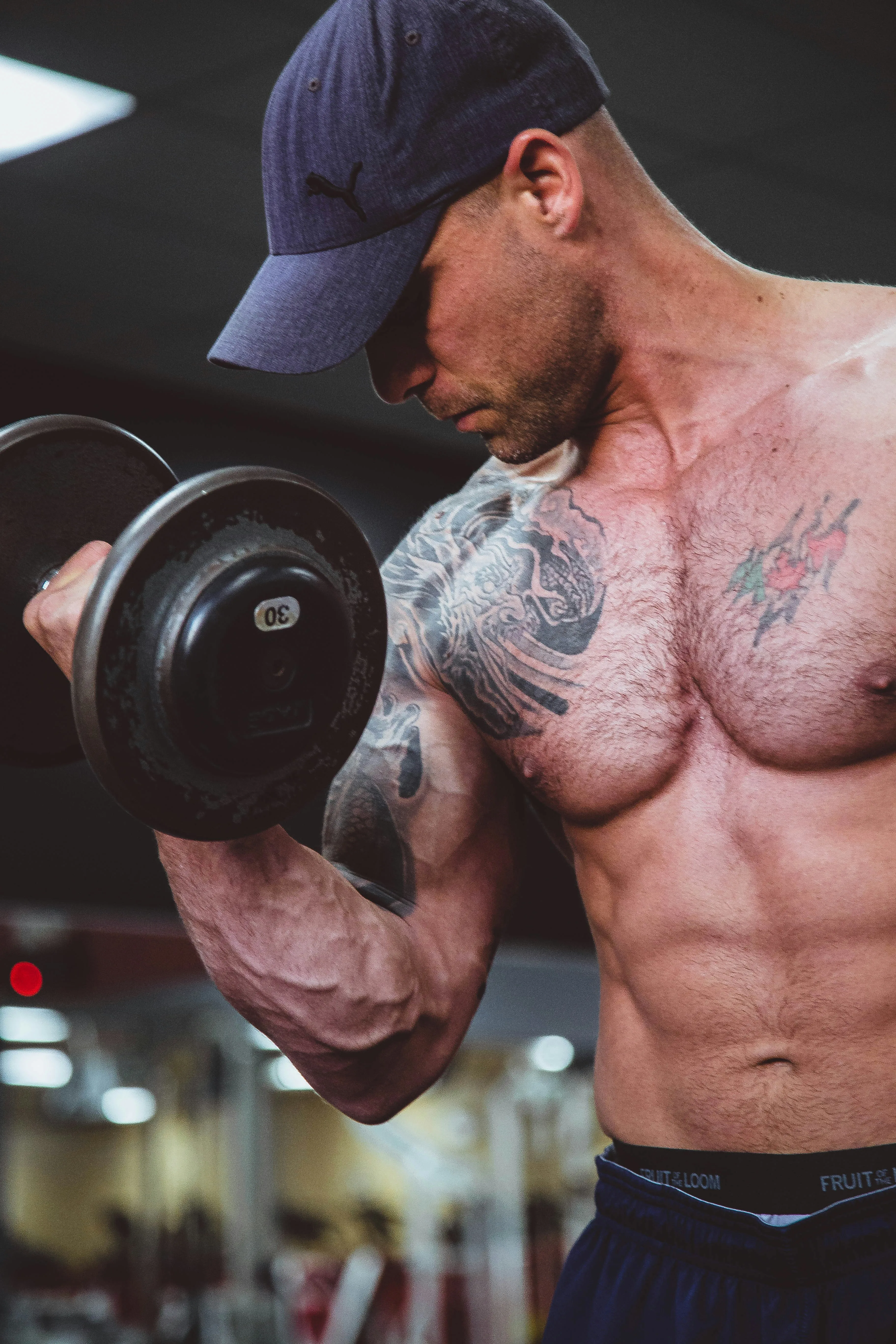 Pratiquant tatoué réalisant un curl biceps avec un haltère de 30 kg en salle de musculation