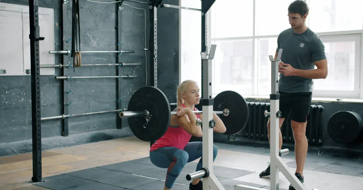 Pratiquante en squat guidée par un coach pour la technique d'exécution